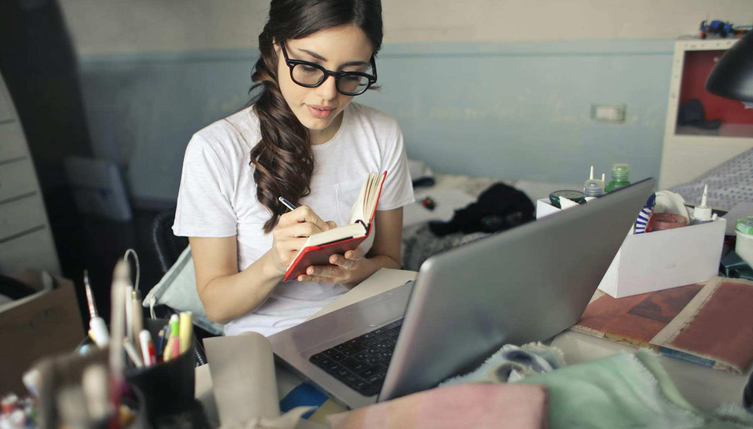 Junge Frau mit Laptop und Notizbuch an ihrem Schreibtisch